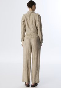 Beige, gestructureerde twee-delige outfit met een lange mouw top en wijde broek met een elastische tailleband. Eenvoudig, strak ontwerp.
