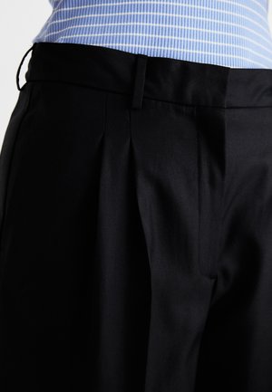 Black tailored trousers featuring a structured waistband, pleat detail, and smooth texture, paired with a light blue striped top.