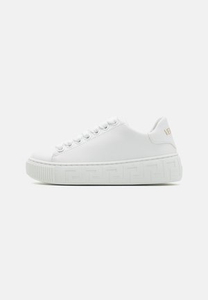 White sneaker made from leather with a textured rubber sole. Features round laces, a smooth upper, and a patterned side panel. Gold logo on heel.