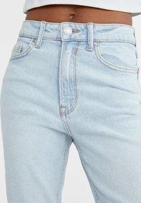 Jeans de tiro alto en azul claro, fabricados en denim, con cierre de botón, costuras visibles y bolsillos frontales con una textura suave.