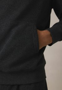 Mørkegrå sweatshirt med tekstureret stof, forlomme og ribbede manchetter og kant. Designet er enkelt og funktionelt.