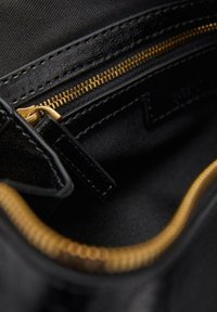 Zwarte stoffen tas binnenkant met een gouden rits, die een gestructureerd oppervlak en nette stiksels langs de randen toont, met een georganiseerd ontwerp.