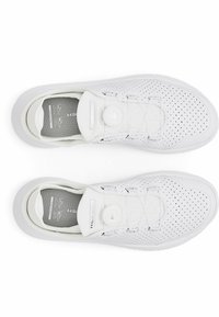 White athletic shoes with perforated design, round fastener, padded collar, and textured insole. Features subtle branding on the tongue.