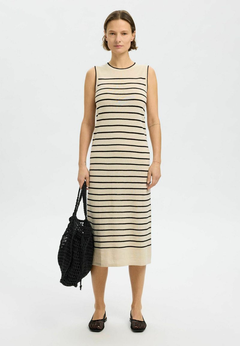 Abito a maglia a righe in beige con strisce orizzontali nere, senza maniche, di lunghezza media, abbinato a una borsa intrecciata nera e scarpe.