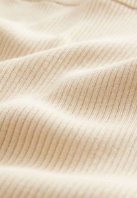 Tissu tricoté côtelé beige doux avec des lignes verticales visibles et de légers plis créant de la texture.