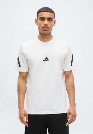 Homme debout face à l'avant, portant un t-shirt blanc Adidas avec des logos noirs sur la poitrine et les manches, et un short noir.