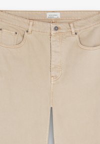 Pantalones recortados beige de mezclilla con cremallera frontal y cierre de botón. Presenta dos bolsillos con detalles de costura en contraste.