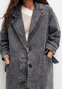 Harmaa farkkutakki rentoa istuvuutta, viistot läpät, kaksi etutaskua ja kolme nappia. Kerroksittain kevyen neuleen päällä.