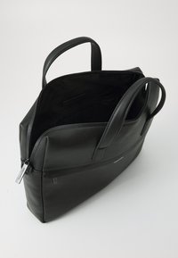 Black leather tote bag featuring a textured finish, dual handles, zip closure, and a spacious interior. Includes branding detail on the side.