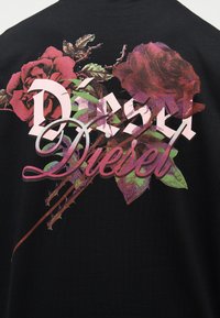 Μαύρο ύφασμα με τυπωμένα ροζ και κόκκινα τριαντάφυλλα και πράσινα φύλλα, επάνω τους μεγάλα στυλιζαρισμένα γράμματα που αναγράφουν "Diesel" και "D'sa".