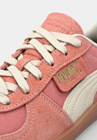 Růžové semišové tenisky s bílými akcenty, obsahující texturované materiály, klasický design na šněrování a zlatou značku na boku.