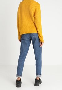 Yellow ribbed sweater, loose fit; paired with blue high-waisted jeans, rolled cuffs; black sneakers complete the outfit.