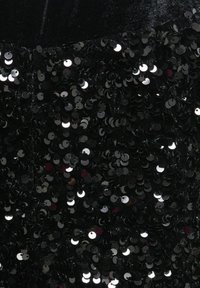 Juoda medžiaga, padengta glaudžiai išdėstytais apskritais blizgučiais, sukuriančiais blizgią, tekstūruotą paviršių, nuo metalinių akcentų atsispindintį šviesą.