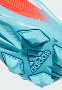 Zatvoren prikaz tirkizne potplate s kopčama s teksturiranim čavlima i Adidas logom u sredini na sportskom čizmu s narančastom mrežastom gornjom.