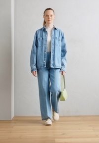 Chaqueta de mezclilla azul claro y pantalones anchos a juego; combinados con una blusa blanca. Bolso verde claro y zapatos blancos; textura suave.
