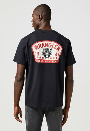 Czarna bawełniana koszulka z dużą czerwoną i białą grafiką na plecach, na której znajduje się tekst "WRANGLER", ilustracja tygrysa oraz gwiazdki.