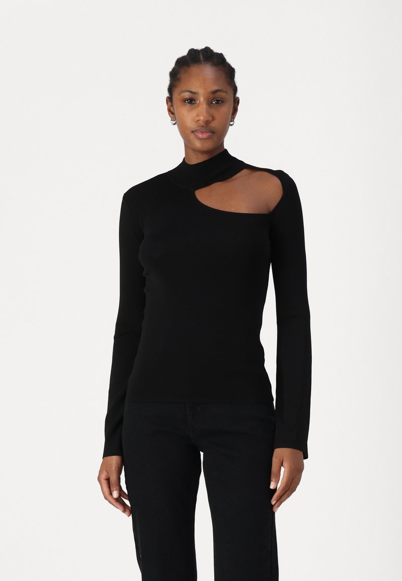 Haut noir à manches longues avec un col montant et une découpe asymétrique sur l'épaule. Matière douce et ajustée. Associé à un pantalon noir.