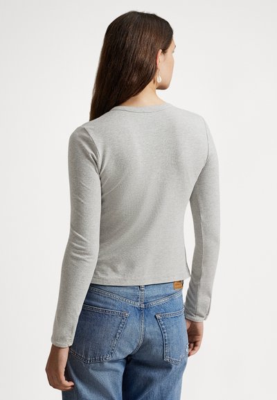 Γκρι cropped top με μακριά μανίκια από μαλακό ύφασμα, διαθέτει στρογγυλή λαιμόκοψη και λεία υφή. Φοριέται με ψηλόμεσο μπλε τζιν.