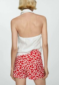 Bílý lněný top s halter výstřihem, doplněný šortkami s červeným květinovým potiskem vyrobenými z lehkého materiálu. Tento outfit má ležérní design.