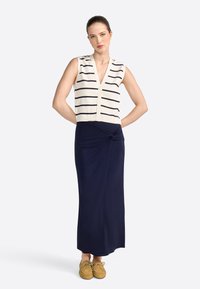 Top senza maniche a righe navy e bianche con bottoni. Gonna fluida navy con un design anteriore annodato. Scarpe beige completano l'outfit.
