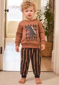 Sweatshirt marron avec un motif dinosaure noir, assorti à un pantalon rayé marron et noir. Tissu doux et décontracté, poignets côtelés pour le confort.