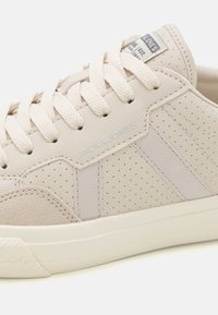 Beez sneaker tekstureeritud nahaga ja perforatsioonidega, beežide paelte ja pehmendatud kraega, küljes "JACK & JONES" brändingu detail.