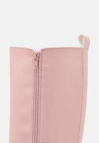 Botín de cuero rosa con cremallera frontal, que presenta una textura suave y una pequeña pestaña blanca en la parte superior.