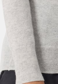 Felpa grigia chiara con un morbido lavoro a maglia testurizzato. Polsini e orlo a coste. Design leggermente accorciato con piccolo taglio laterale sul bordo.