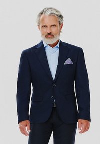 Navy blue marynarka ze dwoma guzikami, kieszeniami z klapkami oraz wzorzystą poszetką. Jasnoniebieska koszula pod spodem. Gładka faktura materiału.