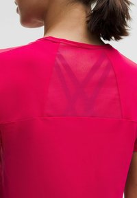Žiarivo ružový športový top s krátkymi rukávmi, s priehľadnou panelou na chrbte a bezešvou konštrukciou pre pohodlie.