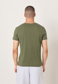 Trumpomis rankovėmis alyvuogių žalia medvilninė marškinėliai, pagaminti iš minkštos medvilnės, su apvalia iškirpte ir paprastu dizainu, matomi iš nugaros.