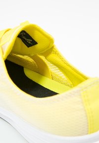 Chaussure à enfiler en maille jaune avec un col rembourré, semelle intérieure noire et semelle extérieure en caoutchouc blanche. Présente une finition texturée et un accent élastique.