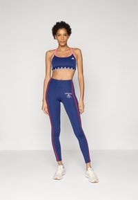 Navy sports bra with pink straps and triangular pattern; matching tight leggings with red side stripes and white branding. Athletic shoes.