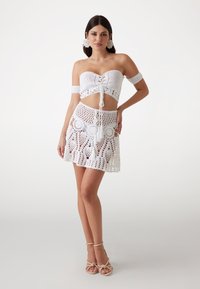 Wit haakwerk twee-delige set met een strapless top met een strik voorkant en een rok met ronde uitsparingen, franjes en opengewerkte details.