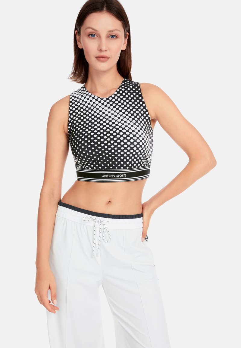 Black and white patterned crop top with a round neckline, featuring a dotted design and a solid black band at the hem. Paired with white pants.