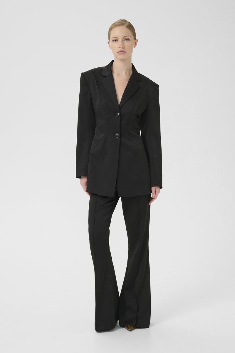 Black tailored suit featuring a structured blazer with sharp shoulders and two buttons, paired with flared pants, all in smooth fabric.