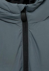 Siva izolirana jakna z črnim sprednjim zadrgo, visokim ovratnikom in kapuco, s gladko površino in šivanim detajlom.