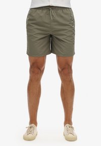 Costumi da bagno verde oliva realizzati in tessuto leggero, dotati di una vita elastica con cordoncino e dettaglio del logo laterale.
