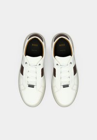 Sneakers in pelle bianca con dettagli marroni testurizzati, punta arrotondata, suola piatta in gomma e design con lacci con etichetta logo sul lato.