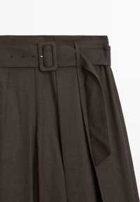 Jupe haute taille marron foncé avec une ceinture à boucle carrée, un design plissé à l'avant et un tissu à texture douce.