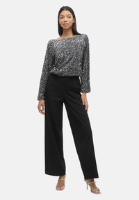 Glanzend zilveren top met lange mouwen, gecombineerd met zwarte wijdvallende broek en metallic strappy hakken. Soepele textuur en eigentijdse silhouet.