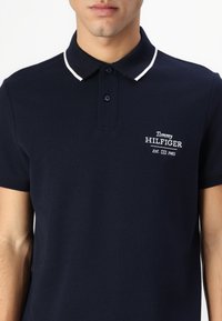 Marineblå polo med tekstur, hvite detaljer på kragen og brodert "Tommy HILFIGER" logo på brystet.