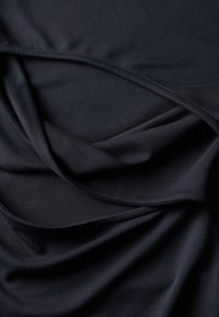 Zwarte stof met een gladde textuur, gedrapeerd om zachte plooien en subtiele schaduwen te creëren, die de vloei en afwerking van het materiaal benadrukken.