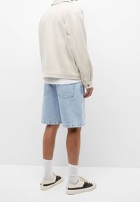 Lyse beige jakke, blå denim shorts og beige sneakers. Funktioner inkluderer klassisk krave, afslappet pasform og rå kant på shorts.