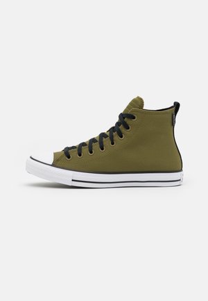 Zielone płótnowe sneakersy za kostkę z czarnymi sznurówkami, białą gumową czubką i kontrastującą czarną paską wzdłuż podeszwy. Posiadają metkę z logo z tyłu.