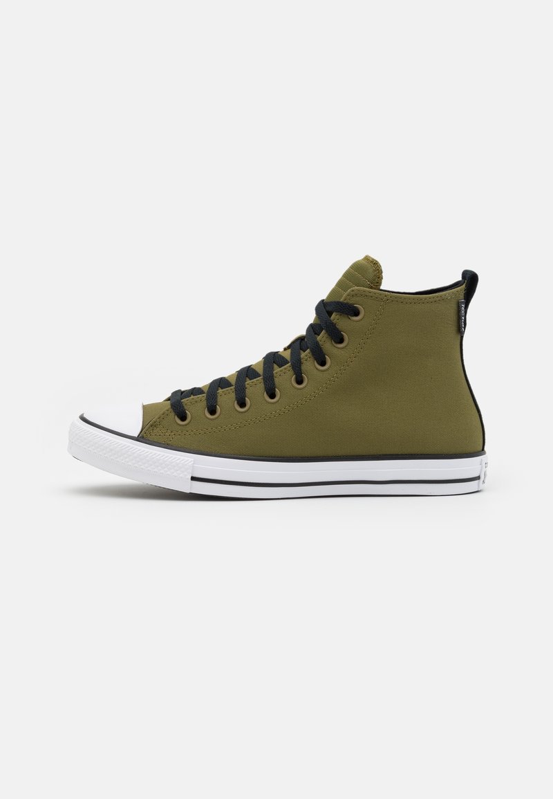 Zelená plátěná vysoce průmyslová teniska s černými tkaničkami, bílým gumovým špičkovým krytem a kontrastním černým pruhem podél podešve. Má logo štítek na zadní straně.