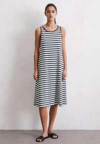 Gestreepte jurk met een mouwloos ontwerp in marineblauw en wit. Kenmerkt zich door een ronde halslijn en een losse silhouette. Draagt met zwarte instapsandalen.
