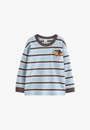 Lille barn iført en langærmet trøje med striber, brune bukser, blå sneakers og en brun strikket hue, går og kigger til siden.