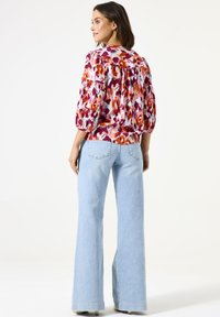 Blusa floral multicolor con mangas abullonadas, combinada con jeans de campana de color azul claro. La blusa tiene un escote redondeado y está hecha de una tela suave.