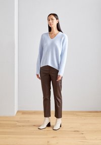 Lyseblå, blød sweater med V-hals og lange ærmer, parret med brune tætsiddende bukser og cremefarvede ankelstøvler med blokhæle.